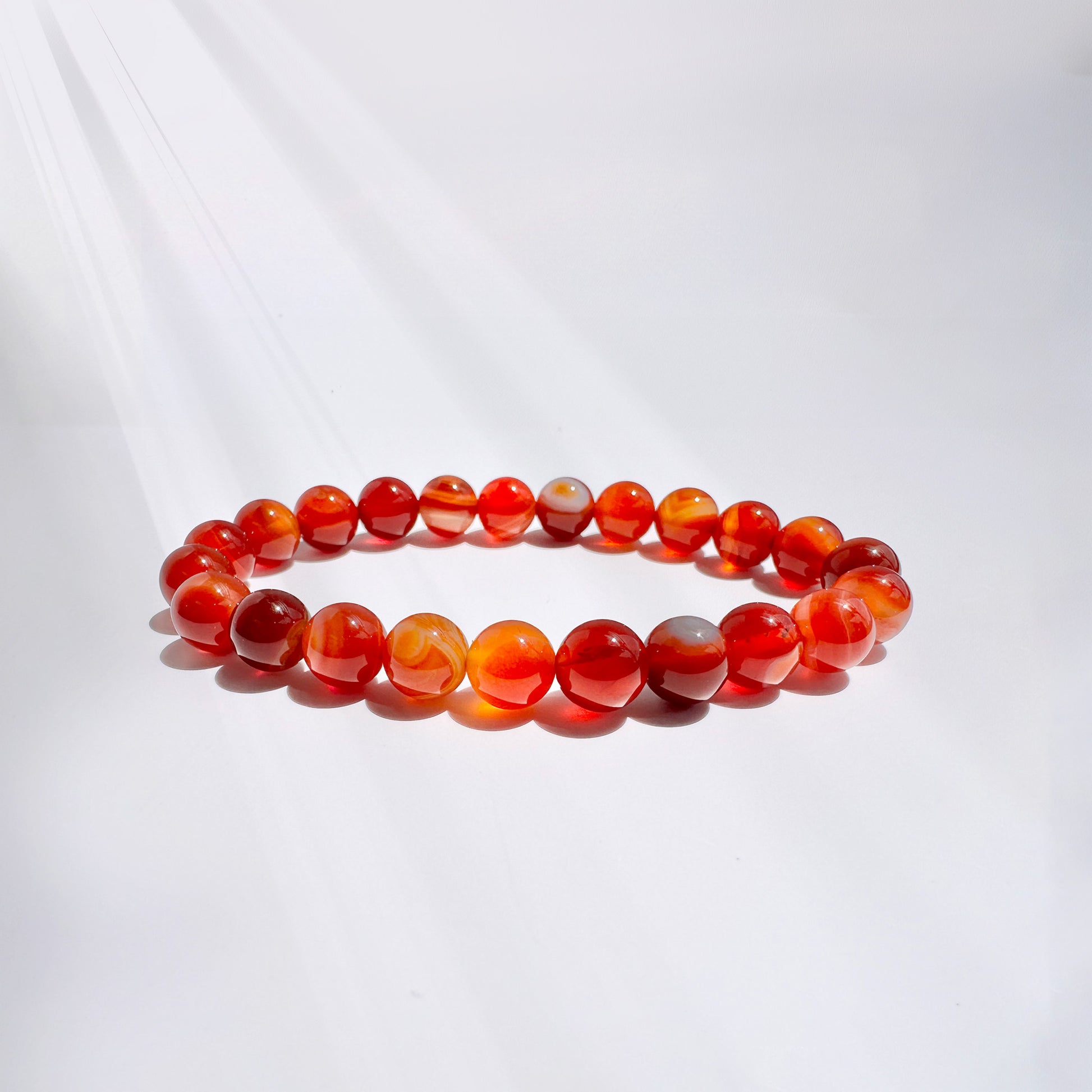 A carnelian bead bracelet featuring 8mm beads, designed to fit petite to medium wrists (5.5" to 6"), displayed on a bracelet stand. Crafted from smooth, vibrant beads, this bracelet embodies courage, confidence, and creativity. The dynamic energy of carnelian infuses the wearer with renewed purpose and ambition, boosting confidence, inspiring creativity, and fueling passion. Ideal for those seeking support on their journey to success, vitality, and self-discovery.