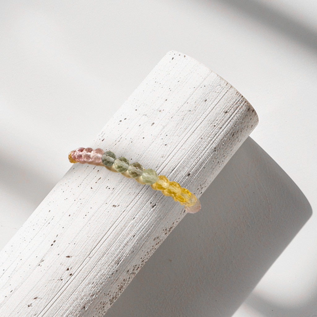 A stack of bracelets made from faceted fluorite beads in magenta, green, yellow, and colorless, displayed on a bracelet stand. Each bead carries unique energies: magenta promotes self-love and emotional healing, green fosters growth and intuition, yellow enhances confidence and creativity, and colorless amplifies the energies of the other beads. These stackable and versatile bracelets elevate any outfit while infusing the wearer's aura with the healing vibrations of fluorite.