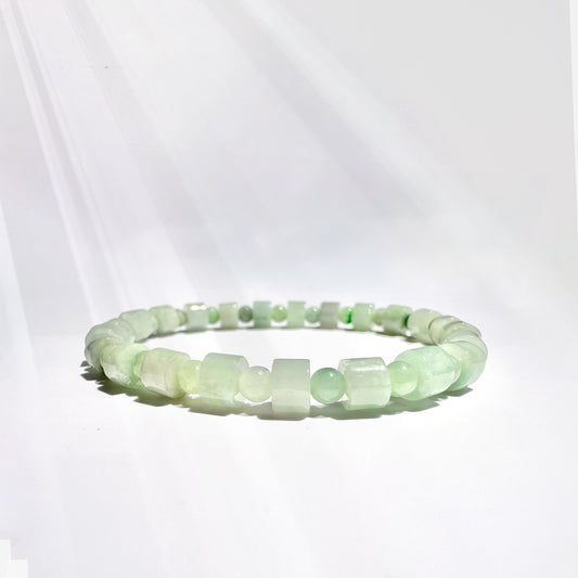 Alt text: A jade bracelet featuring 4mm round beads and 5.5mm square beads, designed to fit petite to medium wrists (5" - 6"), displayed on a bracelet stand. The bracelet blends square beads, symbolizing stability, grounding, and protection, with round beads that represent unity, wholeness, and the infinite cycles of life. This combination creates a powerful synergy that enhances the bracelet's energy, promoting balance, harmony, and spiritual growth