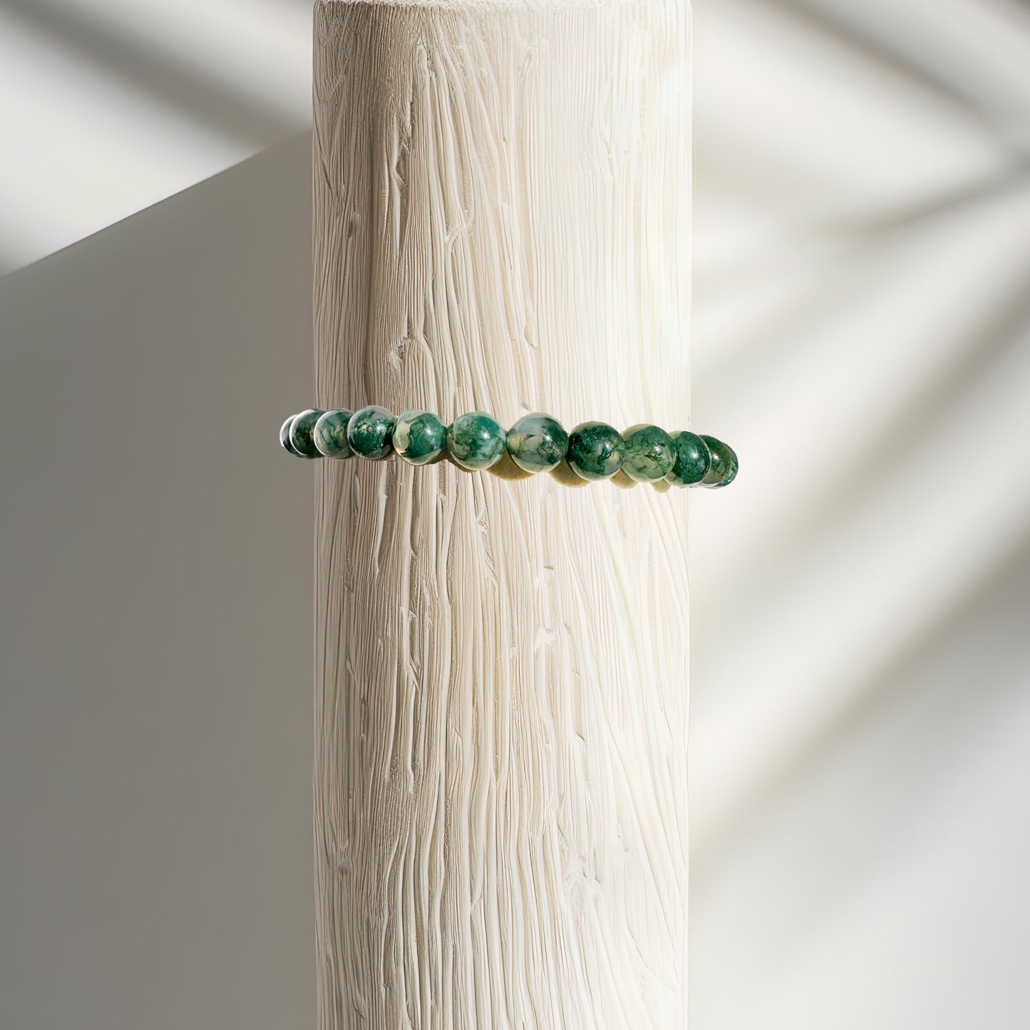 A Moss Agate bracelet displayed on a bracelet stand, known as the "stone of abundance." The bracelet features lush green hues that evoke the tranquility of moss-covered forests. Moss Agate is celebrated for its connection to nature and its ability to attract wealth, prosperity, and success. Its gentle vibrations help clear negativity and stagnant energy, fostering new growth and opportunities.