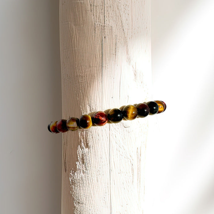 A bracelet crafted from a harmonious blend of yellow, blue, and red tigers eye, displayed on a bracelet stand. This colorful bracelet features yellow tigers eye for confidence and courage, blue tigers eye for clarity and intuition, and red tigers eye for passion and motivation. Together, these stones create a powerful synergy that supports balance, harmony, and empowerment on your spiritual journey.